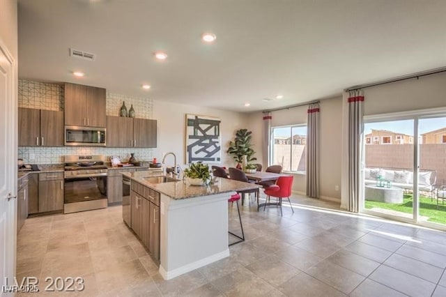 kitchen featuring sink, stainless steel appliances, a kitchen breakfast bar, tasteful backsplash, and an island with sink