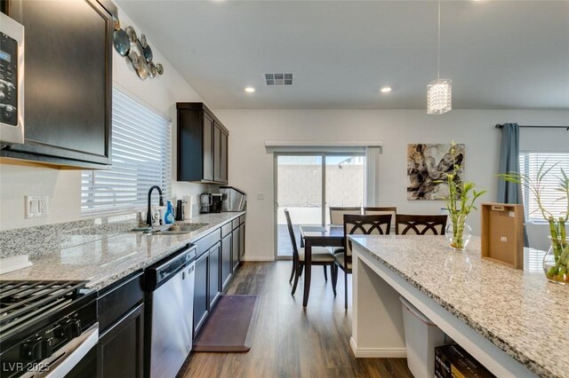 kitchen with hanging light fixtures, light stone countertops, sink, and stainless steel appliances