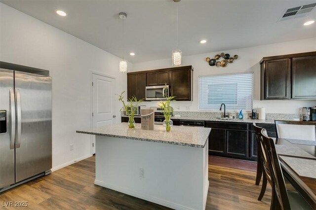 kitchen featuring dark wood-type flooring, sink, hanging light fixtures, appliances with stainless steel finishes, and a kitchen island