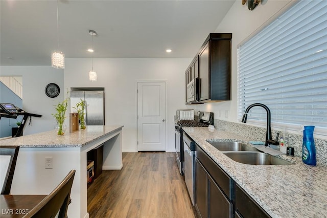 kitchen featuring dark brown cabinets, light wood-type flooring, light stone counters, stainless steel appliances, and a sink