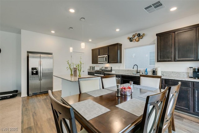 kitchen with stainless steel appliances, a center island, light stone counters, light hardwood / wood-style floors, and decorative light fixtures