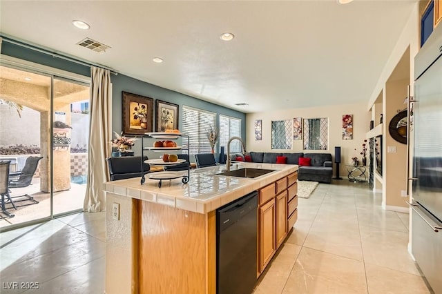 kitchen with built in fridge, dishwasher, sink, a kitchen island with sink, and tile counters