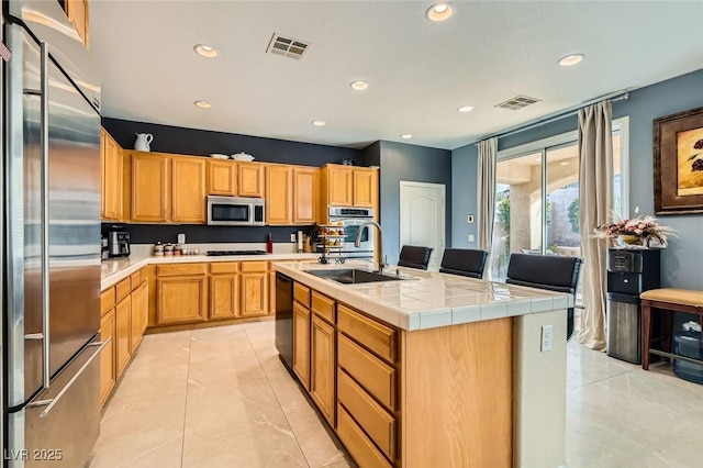 kitchen with an island with sink, stainless steel appliances, tile countertops, and sink