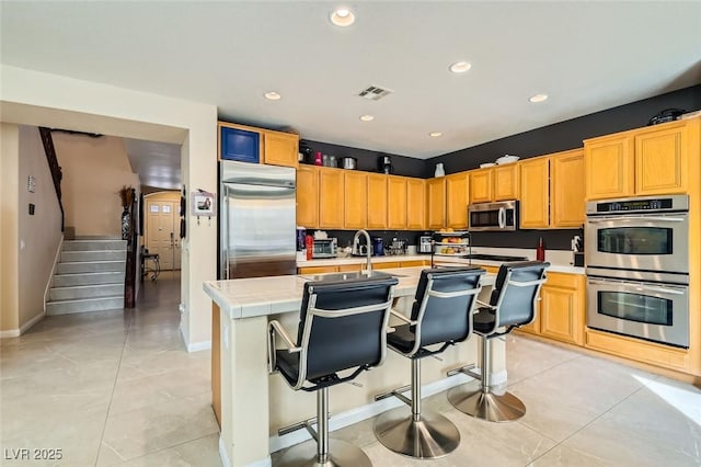 kitchen featuring light tile patterned floors, sink, stainless steel appliances, a kitchen breakfast bar, and a center island with sink