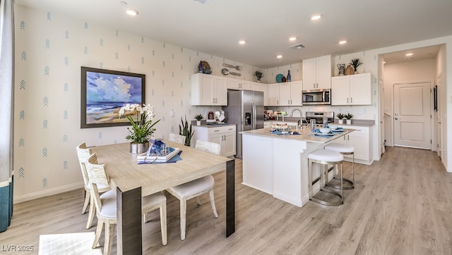 kitchen with white cabinets, appliances with stainless steel finishes, light wood-type flooring, and a center island with sink