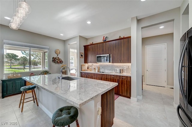 kitchen with a kitchen bar, appliances with stainless steel finishes, sink, hanging light fixtures, and an island with sink