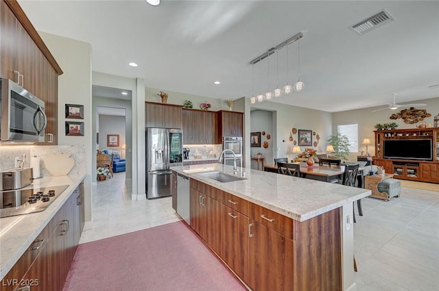 kitchen featuring hanging light fixtures, appliances with stainless steel finishes, backsplash, and a kitchen island with sink