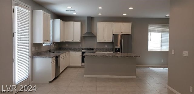 kitchen with white cabinetry, sink, wall chimney range hood, a kitchen island, and appliances with stainless steel finishes