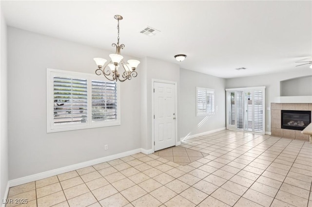 unfurnished dining area featuring light tile patterned flooring, ceiling fan with notable chandelier, and a tiled fireplace