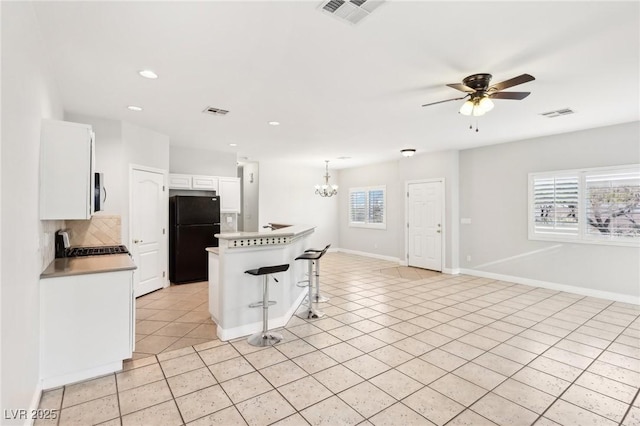 kitchen with white cabinetry, a breakfast bar area, black refrigerator, ceiling fan with notable chandelier, and range