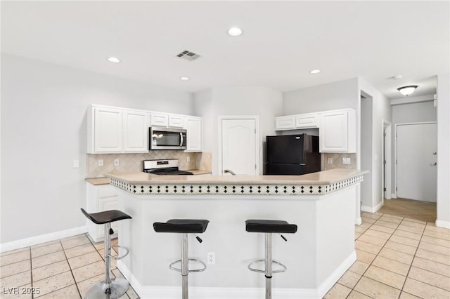 kitchen featuring black refrigerator, a breakfast bar, white cabinets, and white range with electric cooktop