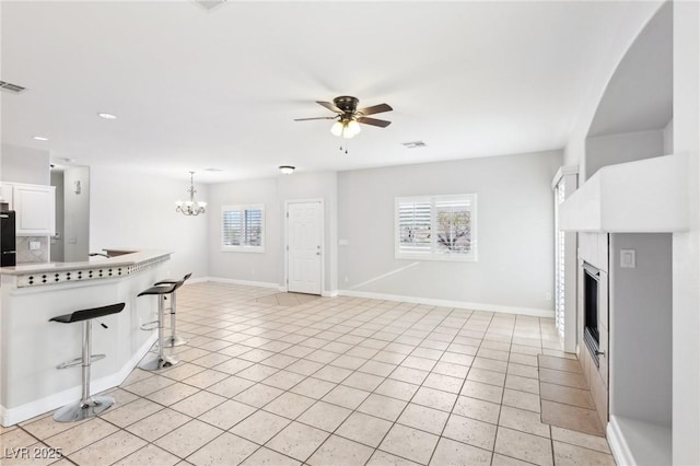 kitchen featuring a breakfast bar, ceiling fan with notable chandelier, decorative light fixtures, plenty of natural light, and white cabinetry