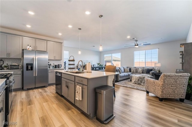 kitchen with appliances with stainless steel finishes, tasteful backsplash, sink, a center island with sink, and gray cabinets