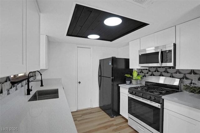 kitchen with sink, light wood-type flooring, appliances with stainless steel finishes, a tray ceiling, and white cabinets