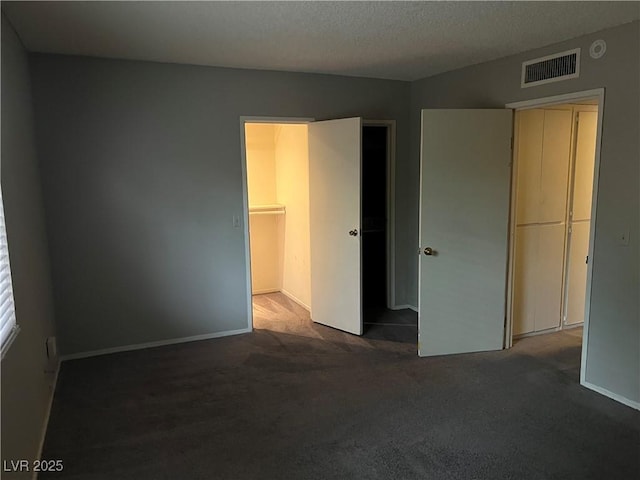 unfurnished bedroom featuring dark carpet, a spacious closet, a textured ceiling, and a closet