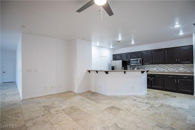 kitchen with ceiling fan, stainless steel appliances, tasteful backsplash, kitchen peninsula, and a breakfast bar area