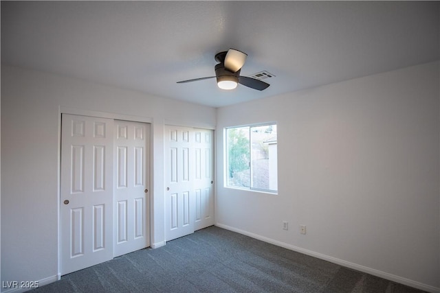 unfurnished bedroom with multiple closets, ceiling fan, and dark carpet