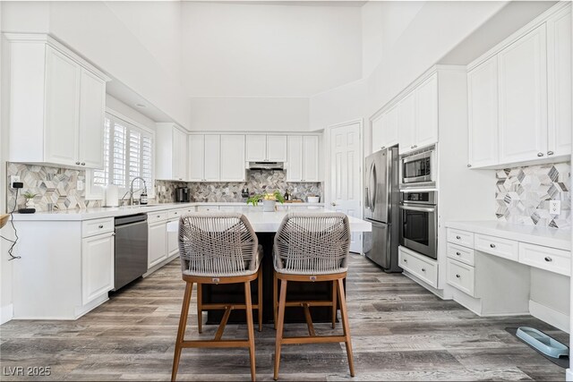 kitchen featuring white cabinets, a center island, a towering ceiling, and stainless steel appliances