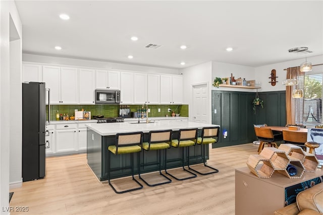 kitchen with a center island with sink, a kitchen breakfast bar, hanging light fixtures, white cabinetry, and stainless steel appliances