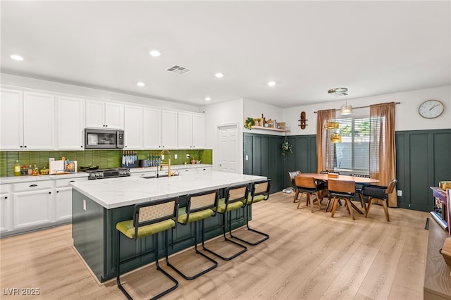 kitchen with white cabinets, stainless steel appliances, a center island with sink, and sink