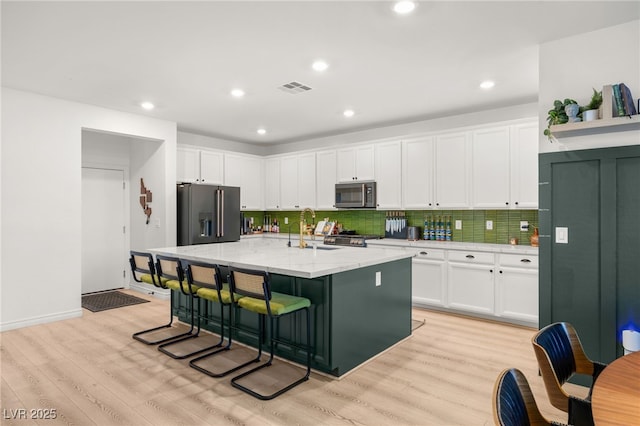 kitchen with appliances with stainless steel finishes, light stone counters, sink, a center island with sink, and white cabinetry