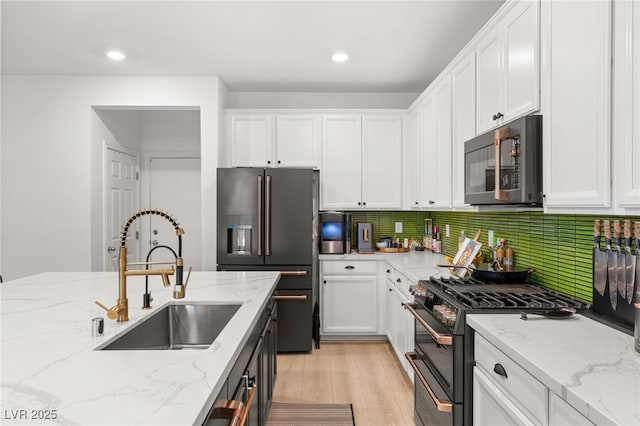 kitchen featuring sink, stainless steel appliances, light stone counters, decorative backsplash, and white cabinets