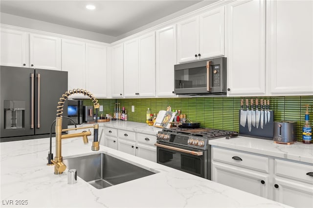 kitchen featuring high quality appliances, sink, white cabinets, and light stone countertops