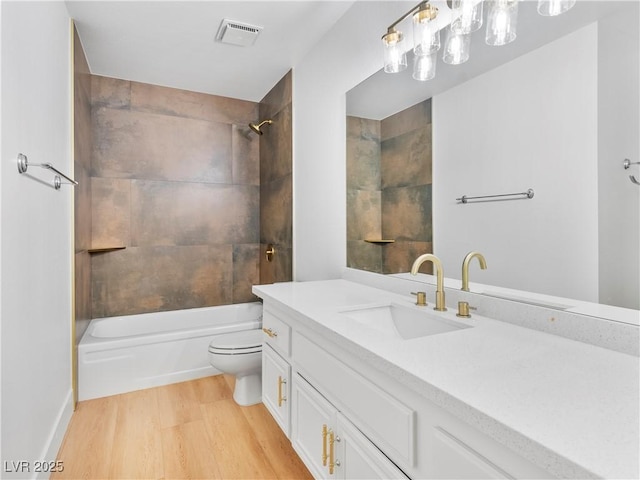 full bathroom featuring vanity, hardwood / wood-style floors, tiled shower / bath combo, and toilet