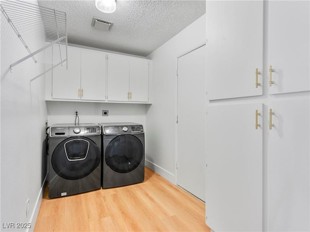 laundry room featuring washer and dryer, cabinets, a textured ceiling, and light wood-type flooring