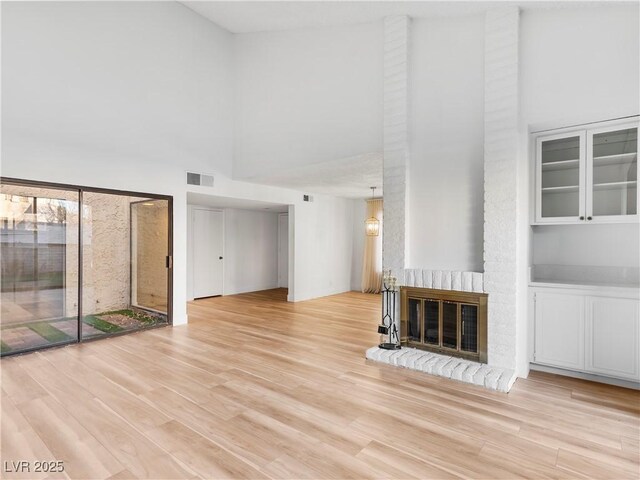 unfurnished living room with a towering ceiling, light hardwood / wood-style floors, and a brick fireplace