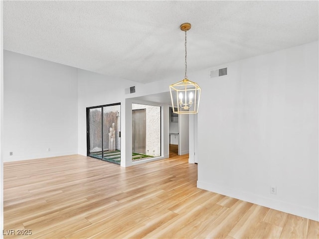 empty room featuring a textured ceiling, wood-type flooring, and a chandelier