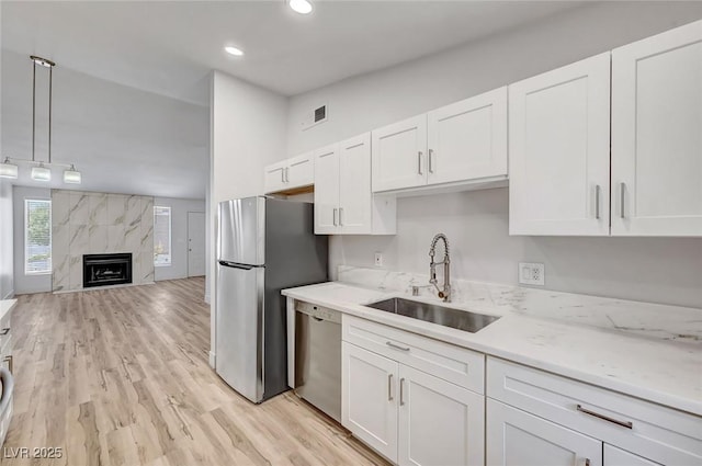 kitchen with sink, a premium fireplace, decorative light fixtures, white cabinets, and appliances with stainless steel finishes