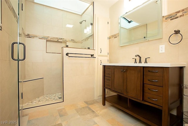 bathroom featuring a skylight, vanity, tile walls, and a shower with shower door