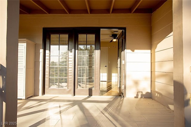 doorway with ceiling fan, light tile patterned floors, and wood walls