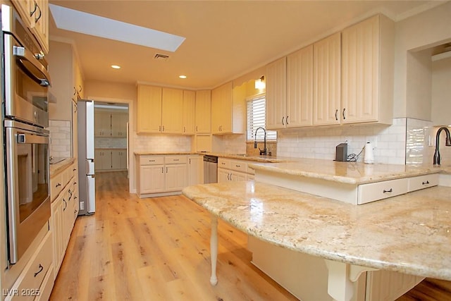 kitchen featuring light stone counters, a skylight, kitchen peninsula, and a breakfast bar area