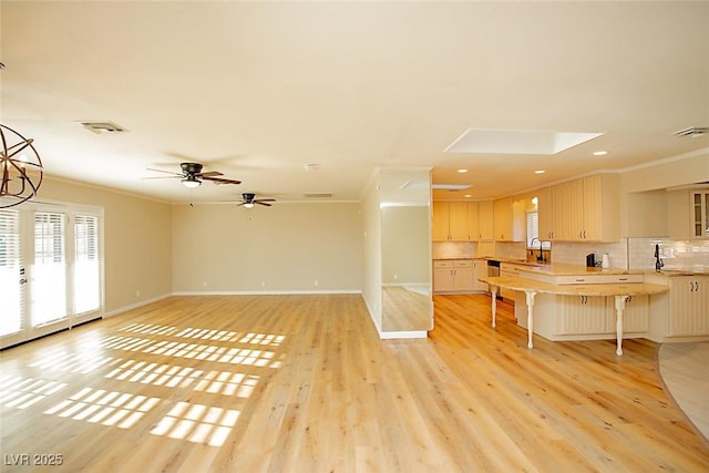 living room featuring crown molding, ceiling fan, light hardwood / wood-style floors, and a skylight