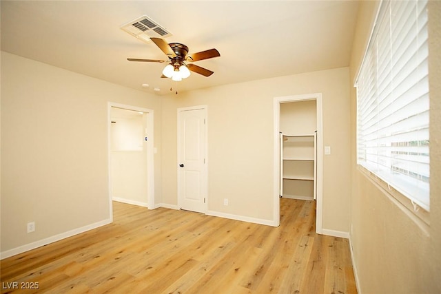 unfurnished bedroom with ceiling fan, a spacious closet, a closet, and light wood-type flooring