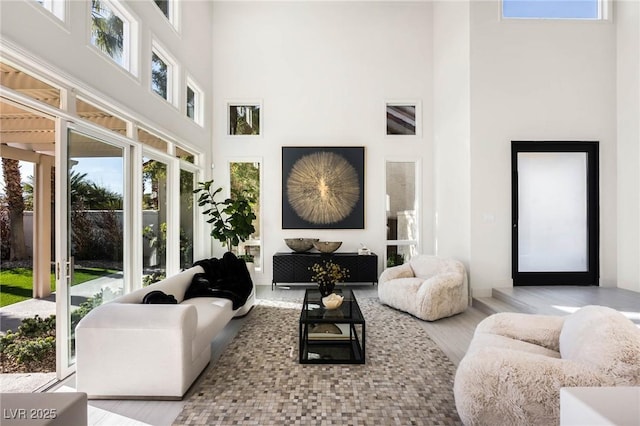 living room with light wood-type flooring, a towering ceiling, and plenty of natural light