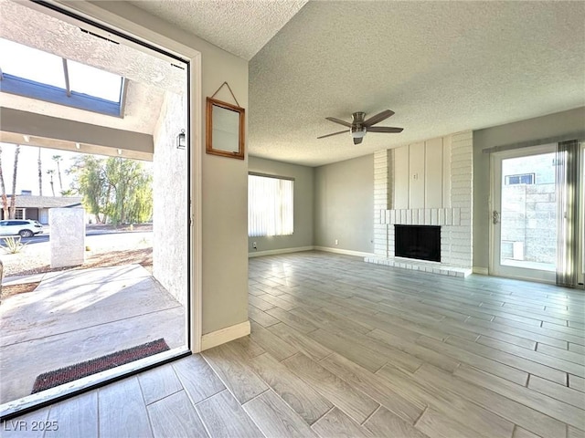 unfurnished living room featuring ceiling fan, a textured ceiling, and a brick fireplace