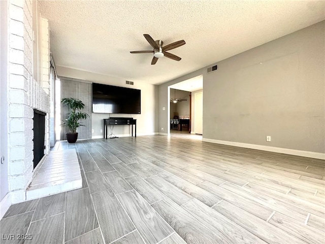 unfurnished living room with ceiling fan, a textured ceiling, and a brick fireplace