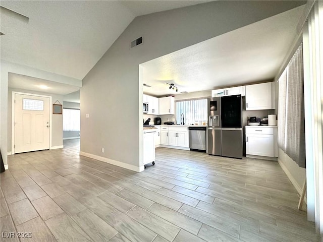 kitchen with sink, vaulted ceiling, stainless steel dishwasher, black fridge with ice dispenser, and white cabinetry