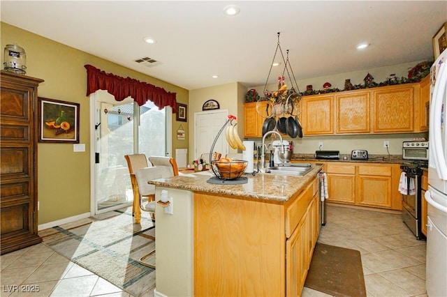 kitchen featuring a breakfast bar, a center island with sink, sink, light tile patterned flooring, and light stone counters