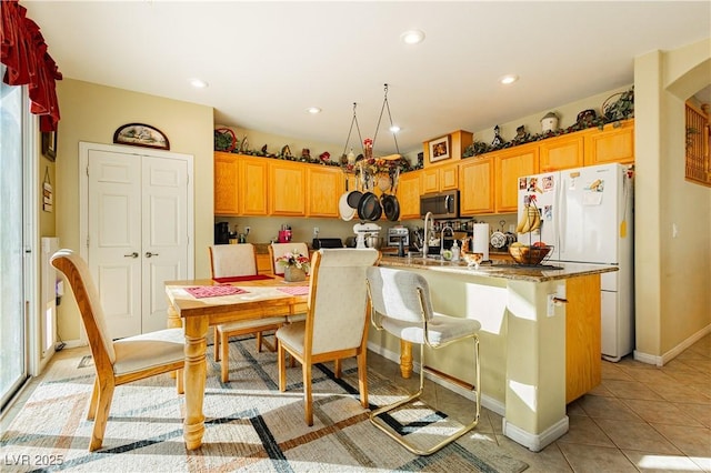 kitchen featuring a breakfast bar, white refrigerator, sink, light tile patterned floors, and an island with sink