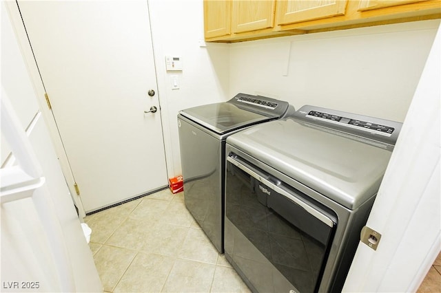 clothes washing area with washing machine and clothes dryer, light tile patterned floors, and cabinets