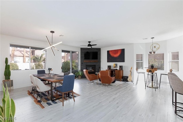 dining room featuring light wood-type flooring, a large fireplace, and ceiling fan with notable chandelier