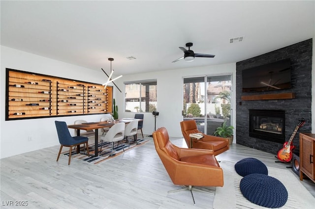 dining space with light wood-type flooring, a stone fireplace, and ceiling fan