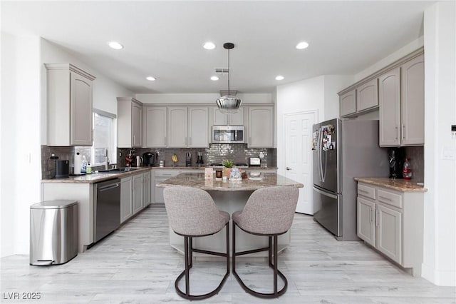 kitchen with sink, hanging light fixtures, gray cabinets, a kitchen island, and appliances with stainless steel finishes