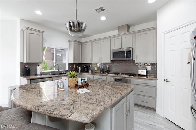 kitchen featuring gray cabinetry, stainless steel appliances, light stone counters, pendant lighting, and a kitchen island