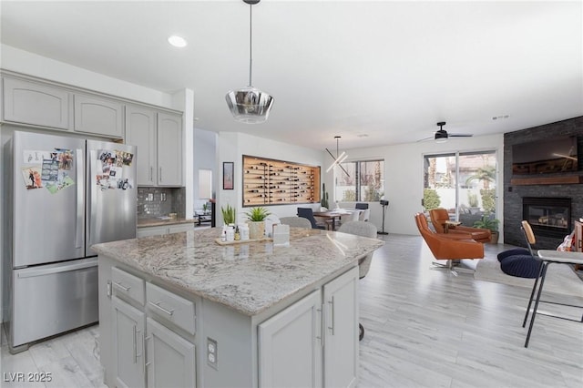 kitchen with stainless steel fridge, tasteful backsplash, ceiling fan, decorative light fixtures, and a center island