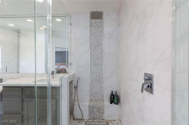 bathroom with a tile shower, vanity, and tile walls